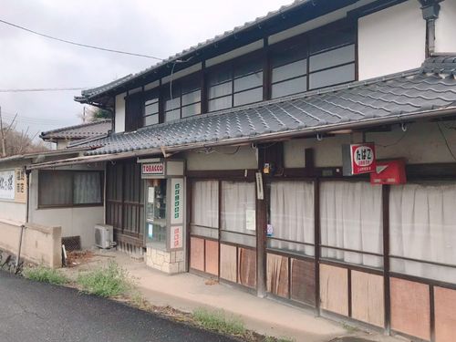 空き家の外観。横に長く店舗部分にはたばこBOXや看板などお店の名残が。木枠の引き戸がレトロです。