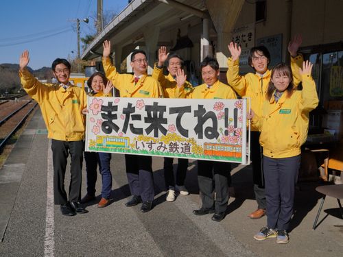 本社がある大多喜駅での列車のお見送りシーンです。手作りの『また来てね！！』横断幕を掲げて笑顔で温かくお見送りしています。