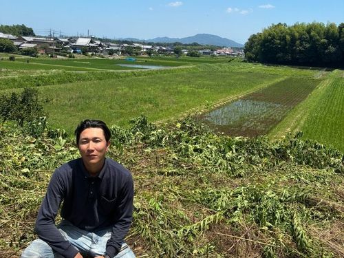 地域おこし協力隊の吉田さん　背景は吉田さんが耕している田畑