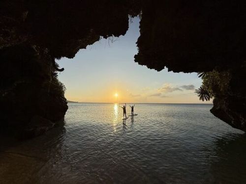 洞窟越しに望む美しい夕日と、水面でSUPを楽しむ幻想的な景色